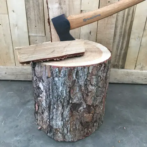 A hardwood chopping block with an axe and a split piece of kindling on top