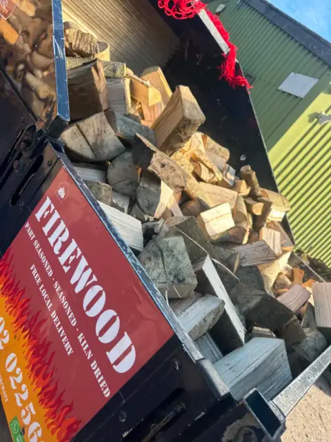 The Woodland Firewood delivery truck loaded with logs, with its red FIREWOOD sign on the side